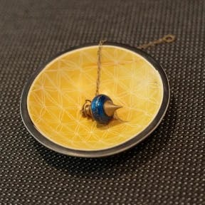 Pendule sur fond doré symbolisant la connexion naturelle et la recherche de l'équilibre intérieur avec Innerflow, spécialiste en hypnothérapie et magnétisme.